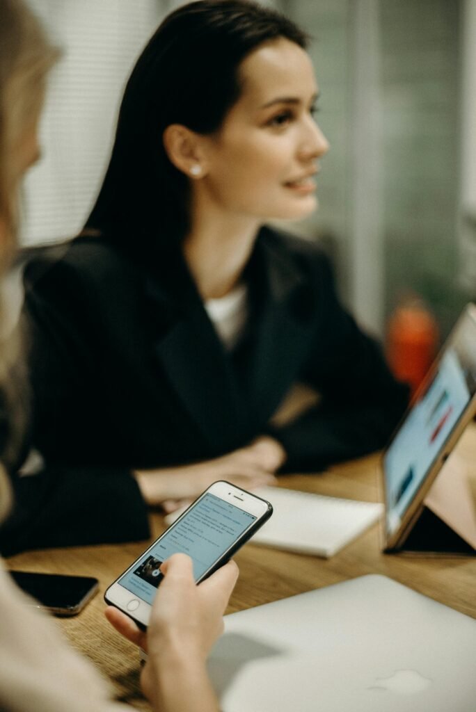 Two women in a meeting using smartphones and tablets in an office setting.